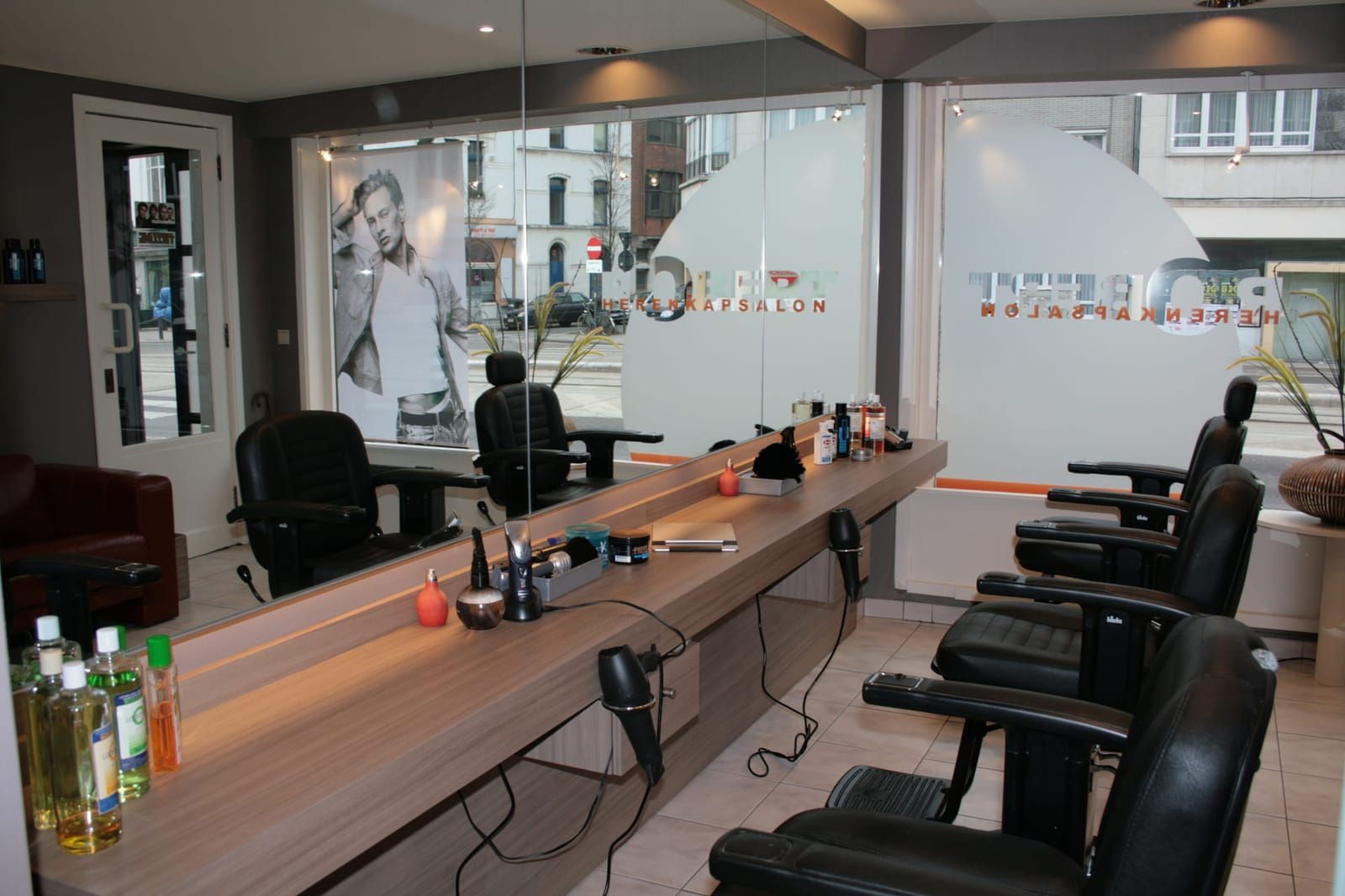 Het salon van Kapsalon Robert: zwarte kappersstoelen langs de spiegelwand, met het ROBERT-cirkelvinyl op de etalageramen