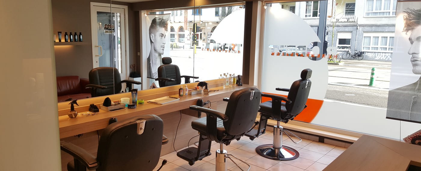 Kappersstoelen langs de werkbank van Kapsalon Robert, met het oranje cirkelvinyl op het etalageraam